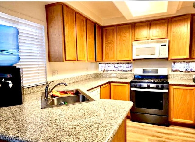 kitchen with light stone counters, kitchen peninsula, sink, light hardwood / wood-style flooring, and gas stove