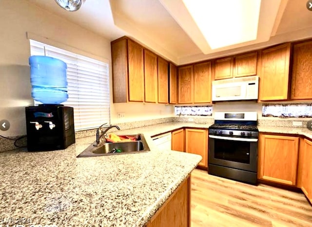 kitchen with light wood-type flooring, white appliances, light stone countertops, and sink