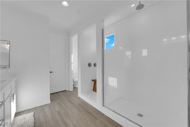 bathroom with toilet, wood finished floors, vanity, a walk in shower, and recessed lighting