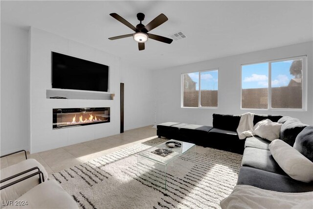 living room featuring light tile patterned flooring, a glass covered fireplace, visible vents, and a ceiling fan