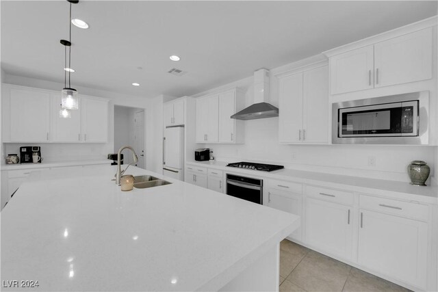 kitchen featuring white cabinetry, stainless steel appliances, decorative light fixtures, sink, and wall chimney range hood