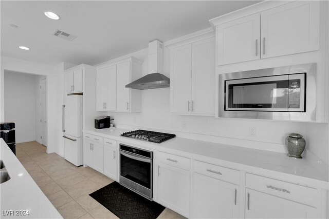 kitchen with light tile patterned floors, wall chimney exhaust hood, white cabinetry, stainless steel appliances, and light stone countertops