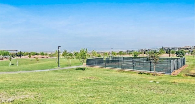 view of tennis court with a residential view, a lawn, and fence