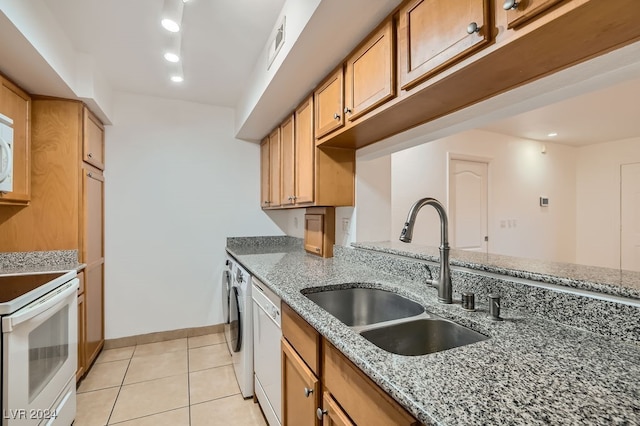 kitchen with light tile patterned flooring, separate washer and dryer, white appliances, light stone countertops, and sink