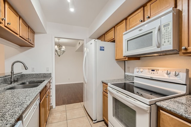 kitchen with light stone counters, white appliances, light tile patterned floors, sink, and a chandelier