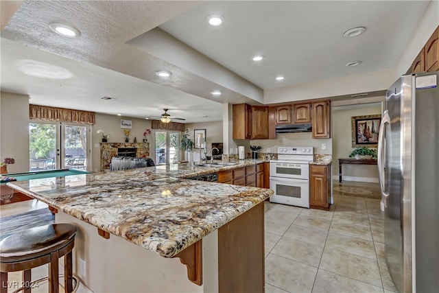 kitchen with ceiling fan, kitchen peninsula, stainless steel refrigerator, a kitchen breakfast bar, and white electric stove