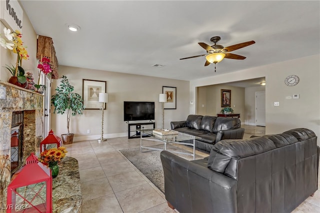 living room with light tile patterned floors, a stone fireplace, and ceiling fan