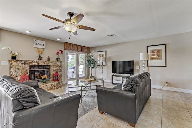 living room with ceiling fan, light tile patterned floors, and a stone fireplace