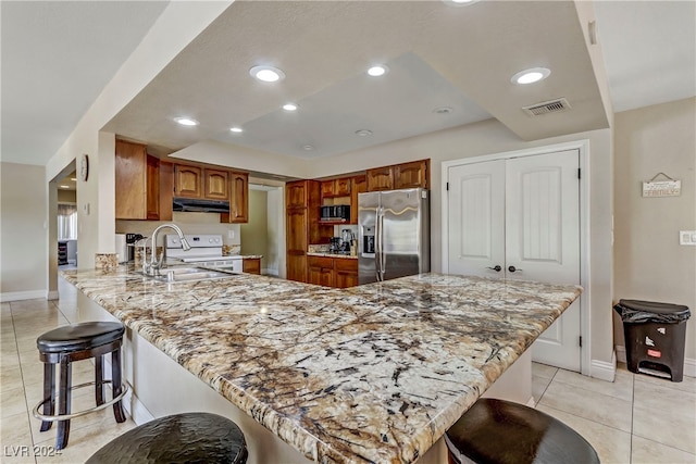 kitchen featuring appliances with stainless steel finishes, a breakfast bar, kitchen peninsula, light stone countertops, and light tile patterned floors