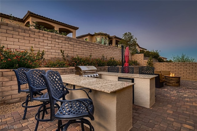 patio terrace at dusk with an outdoor bar, area for grilling, and an outdoor kitchen