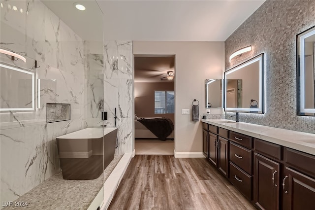 bathroom with tile walls, wood-type flooring, a tub to relax in, and vanity