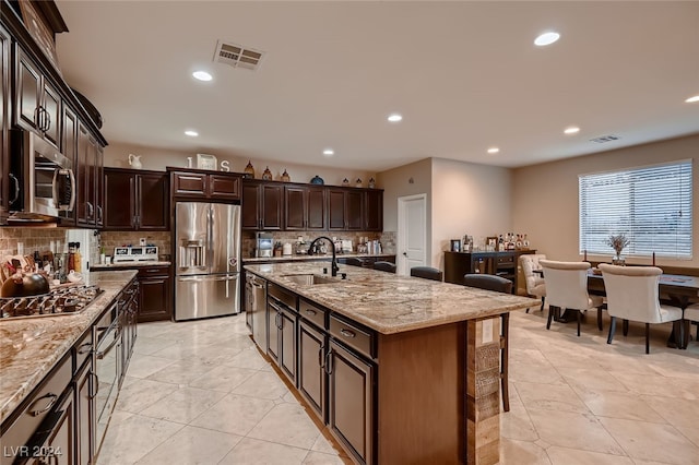 kitchen featuring appliances with stainless steel finishes, light stone countertops, sink, and an island with sink