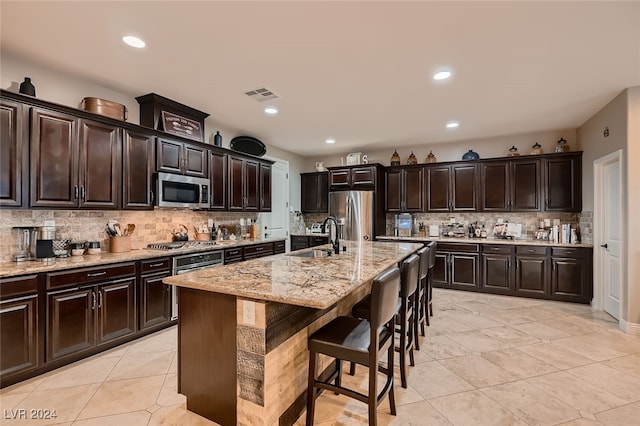 kitchen featuring appliances with stainless steel finishes, decorative backsplash, dark brown cabinetry, a center island with sink, and sink