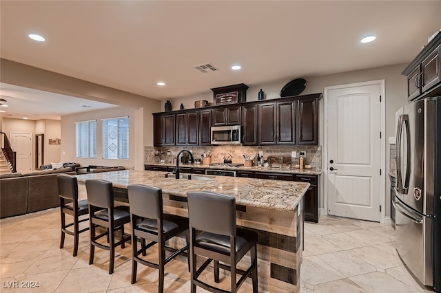 kitchen featuring an island with sink, backsplash, light stone countertops, and stainless steel appliances