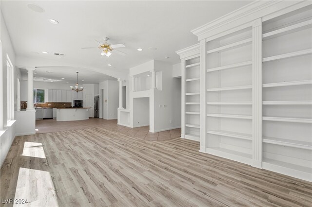 unfurnished living room featuring ceiling fan with notable chandelier, light hardwood / wood-style floors, and ornate columns