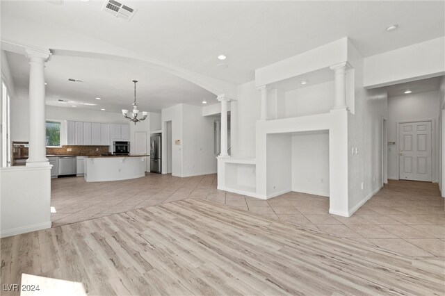 unfurnished living room with light hardwood / wood-style floors, a chandelier, and ornate columns