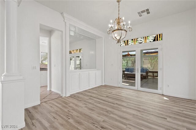 unfurnished dining area with a notable chandelier, light hardwood / wood-style flooring, and ornate columns