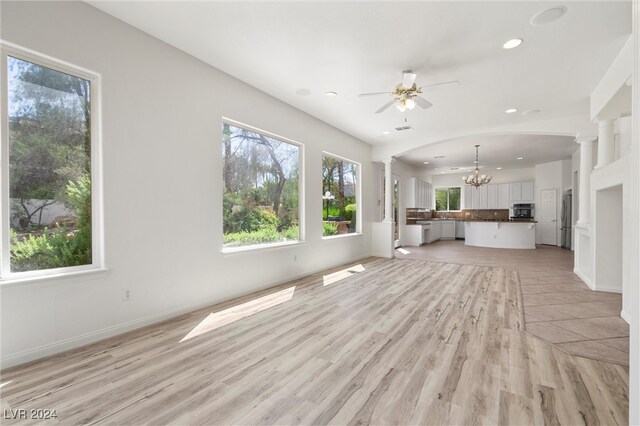 unfurnished living room featuring light hardwood / wood-style flooring, decorative columns, and ceiling fan with notable chandelier