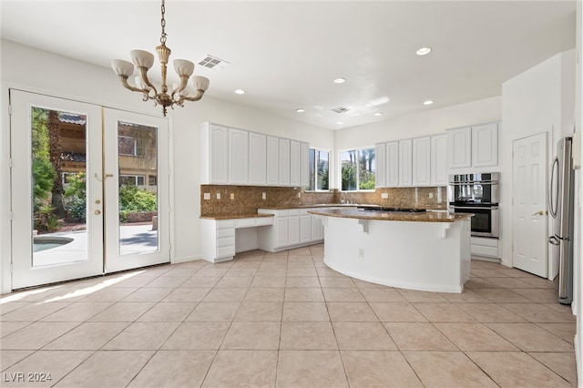 kitchen featuring white cabinets, hanging light fixtures, a kitchen island, stainless steel appliances, and backsplash