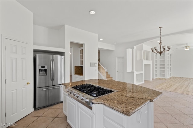 kitchen with appliances with stainless steel finishes, white cabinets, light stone countertops, light tile patterned floors, and decorative light fixtures