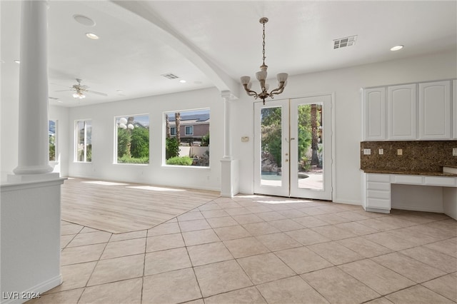 unfurnished living room featuring ceiling fan with notable chandelier, decorative columns, and light hardwood / wood-style floors