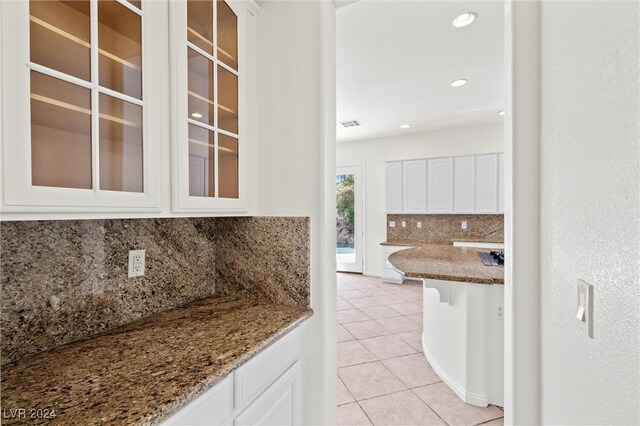 kitchen featuring light stone countertops, backsplash, light tile patterned floors, and white cabinetry