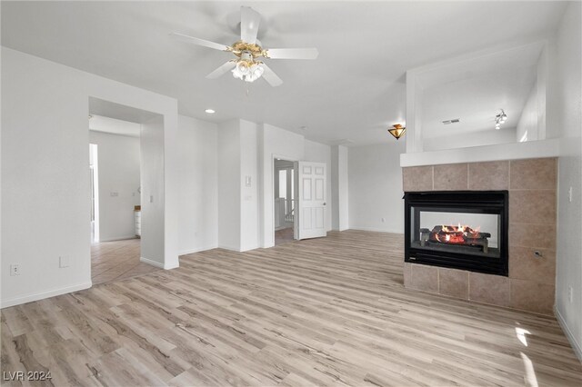 unfurnished living room featuring ceiling fan, light wood-type flooring, a fireplace, and tile walls