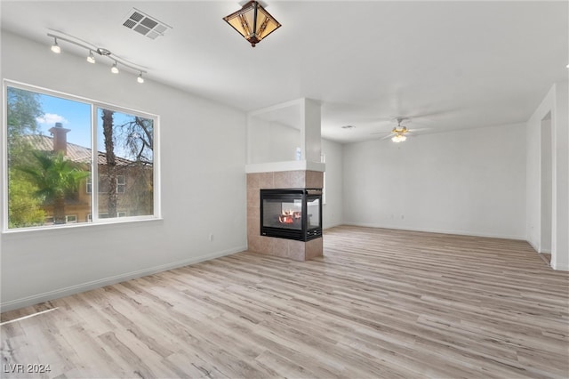 unfurnished living room featuring ceiling fan, a tiled fireplace, and light hardwood / wood-style floors