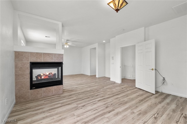 unfurnished living room featuring light wood-type flooring, a tiled fireplace, ceiling fan, and tile walls