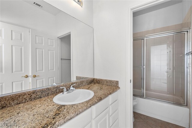 full bathroom with bath / shower combo with glass door, vanity, tile patterned flooring, and toilet