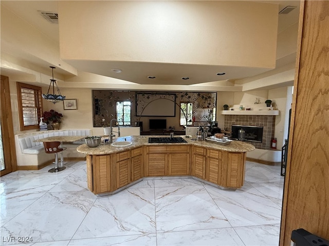 kitchen with kitchen peninsula, a tiled fireplace, pendant lighting, a towering ceiling, and sink