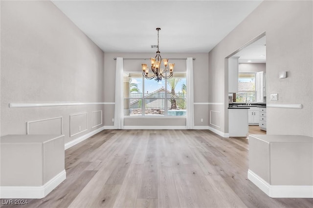 unfurnished dining area with light hardwood / wood-style floors, a healthy amount of sunlight, and a notable chandelier