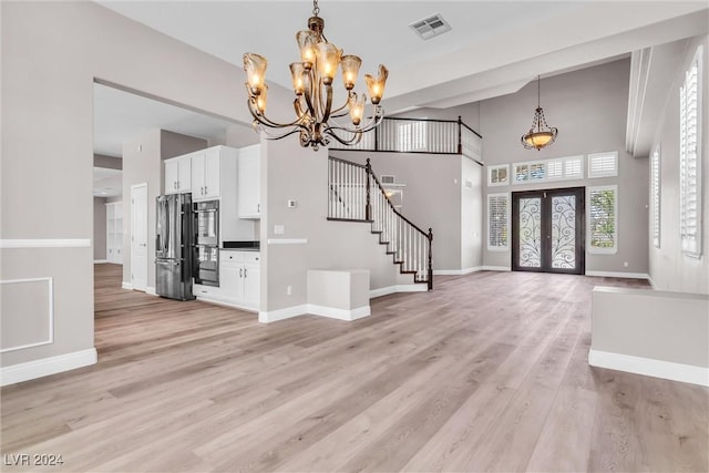 entryway featuring french doors, a towering ceiling, light hardwood / wood-style floors, and a notable chandelier