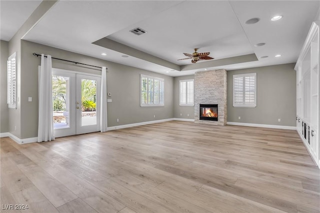 unfurnished living room with a raised ceiling, a fireplace, french doors, and light wood-type flooring