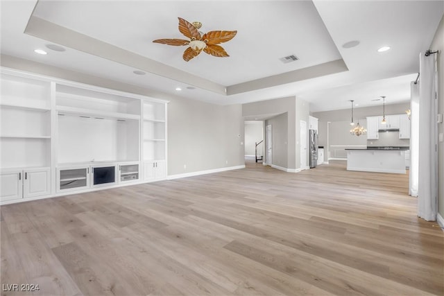 unfurnished living room with a tray ceiling, ceiling fan, built in features, and light wood-type flooring