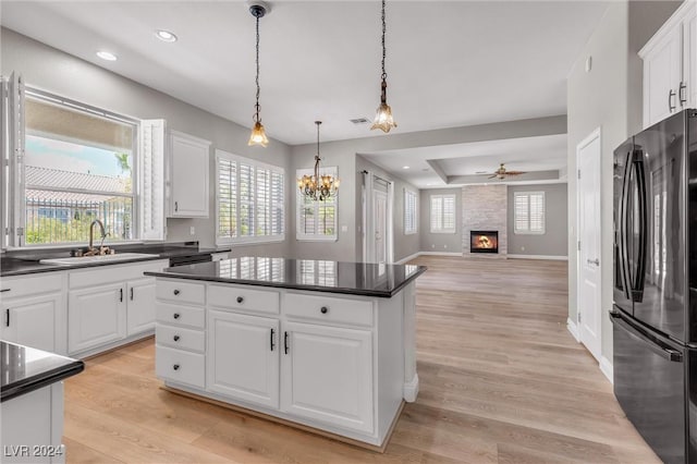 kitchen featuring white cabinetry, a fireplace, black fridge, and sink