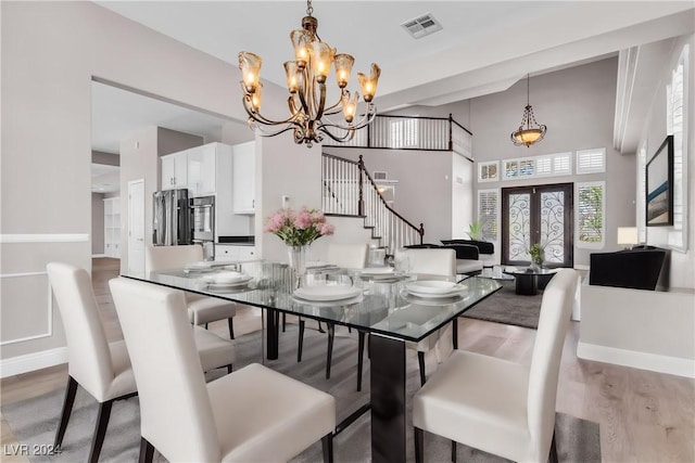 dining space featuring french doors, hardwood / wood-style flooring, a notable chandelier, and a high ceiling