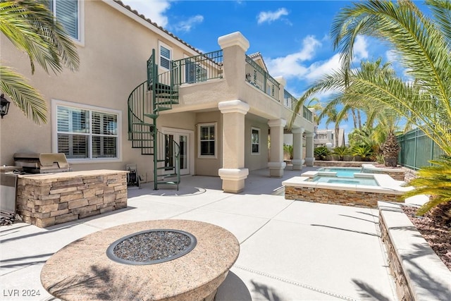 rear view of property with an outdoor fire pit, a balcony, area for grilling, an in ground hot tub, and a patio