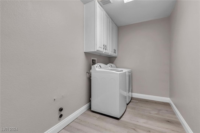 clothes washing area featuring washer and dryer, cabinets, and light hardwood / wood-style flooring