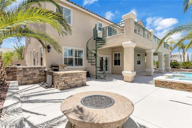 rear view of house featuring exterior kitchen, a fire pit, a balcony, an in ground hot tub, and a patio