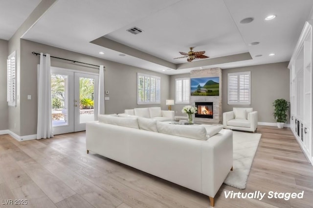 living room with french doors, a large fireplace, light hardwood / wood-style floors, and a raised ceiling