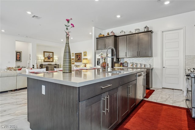 kitchen with dark brown cabinets, a kitchen island with sink, backsplash, and sink