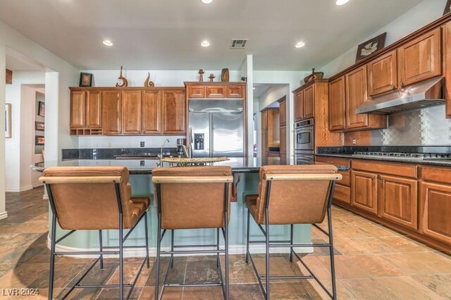 kitchen featuring stainless steel appliances, tasteful backsplash, a breakfast bar, and a center island with sink