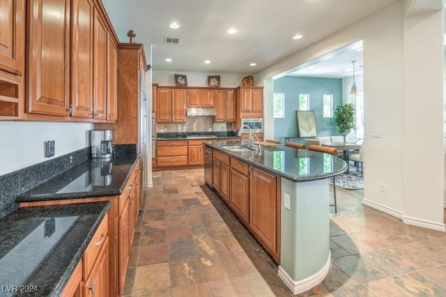 kitchen with sink, dark stone countertops, a center island with sink, decorative backsplash, and stainless steel dishwasher