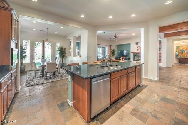 kitchen featuring decorative light fixtures, dishwasher, sink, dark stone countertops, and a kitchen island with sink