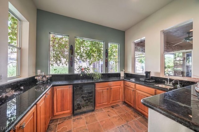 kitchen with wine cooler, ceiling fan, dark stone counters, and sink