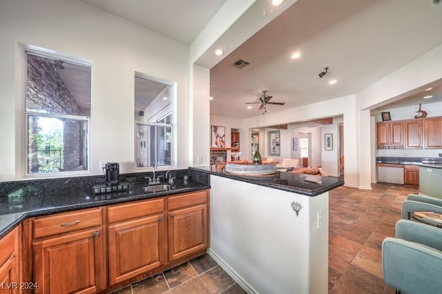 kitchen featuring dark stone countertops, sink, kitchen peninsula, and ceiling fan