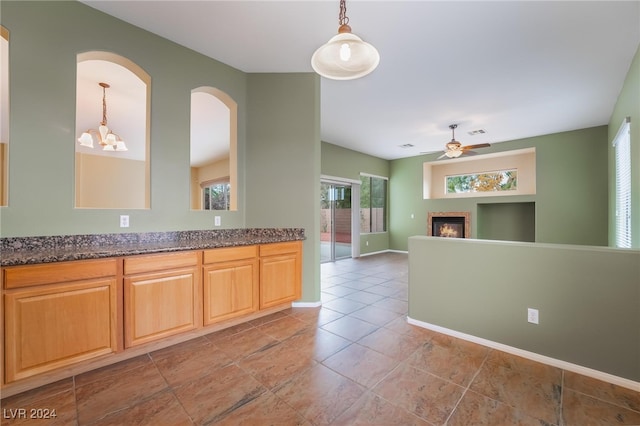 kitchen featuring ceiling fan with notable chandelier, decorative light fixtures, dark stone counters, and light tile patterned flooring