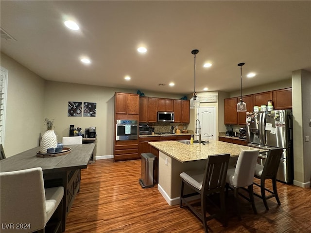 kitchen with appliances with stainless steel finishes, hanging light fixtures, a breakfast bar, dark hardwood / wood-style floors, and sink