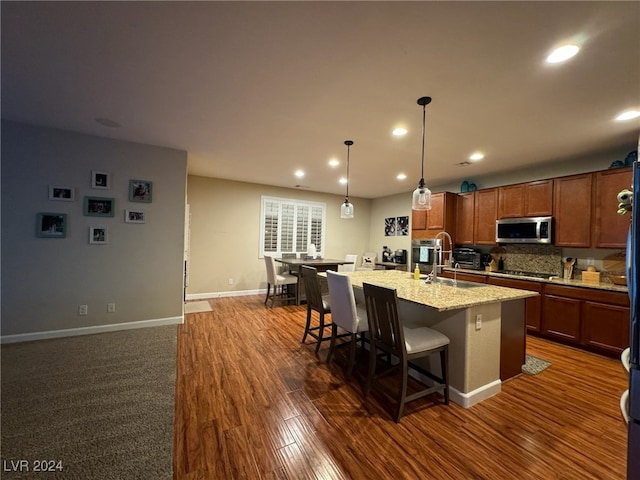 kitchen featuring light stone counters, dark wood-type flooring, a kitchen island with sink, sink, and a kitchen bar